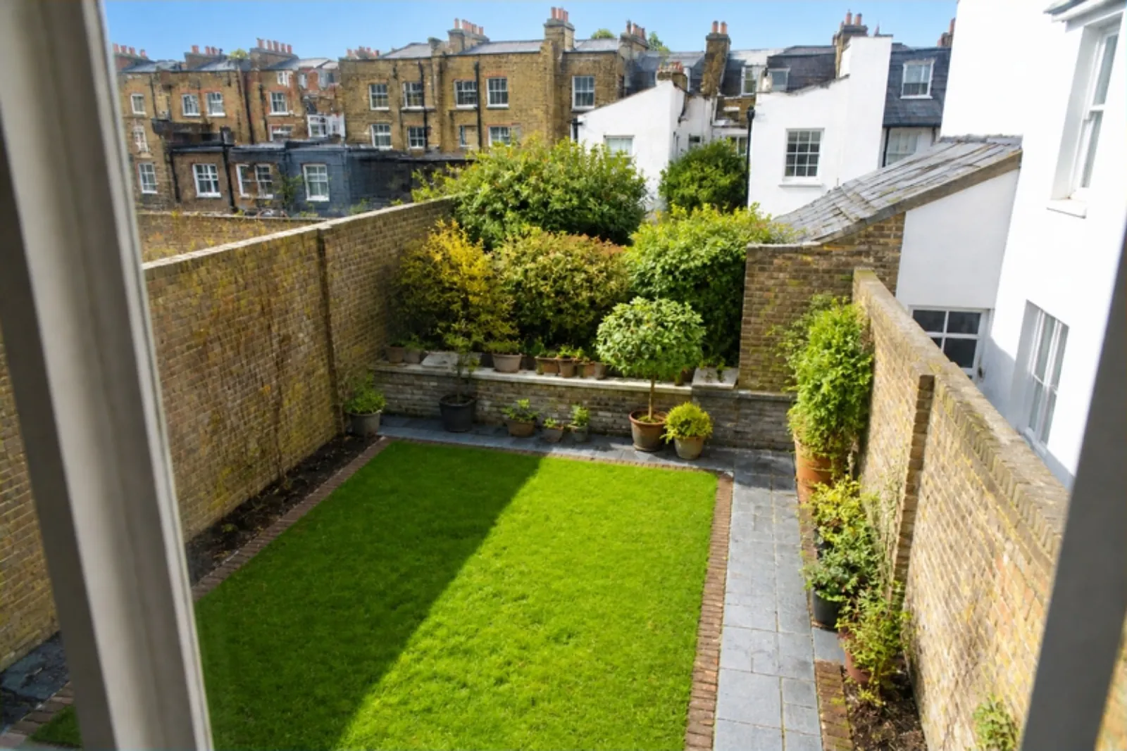 Upstairs view over a small walled courtyard lawn with a slate path and pots, city rooftops beyond